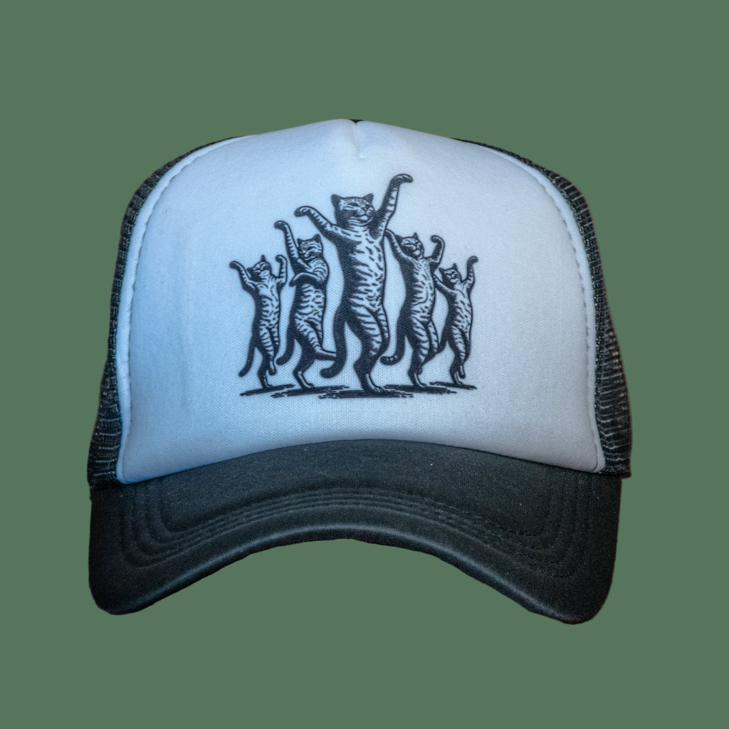 White cap with black mesh and embroidered design of five cats on a wooden surface.