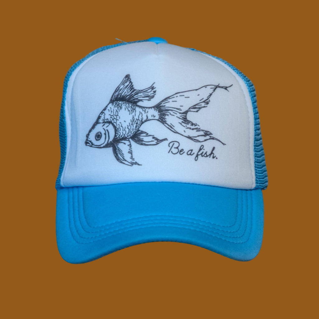 Blue and white cap with fish illustration and 'Be a fish' text on a wooden surface.